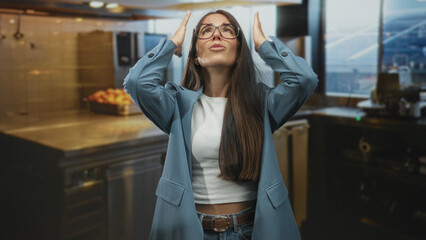 Woman with glasses hands to head near airport window and counter, wearing blazer and jeans, raised arms and worried expression; frustration.