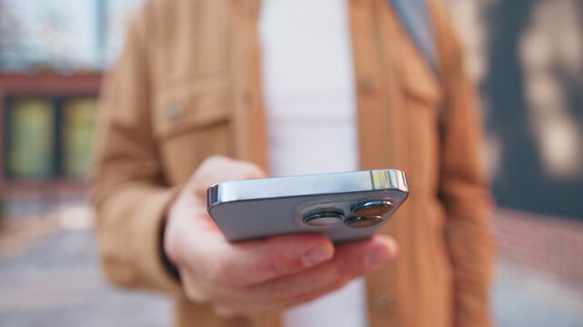 Close camera view person holding smartphone and entering information by tapping on touch screen. Focus on top edge of device while user standing outside. Detailed shot capturing simple interaction.