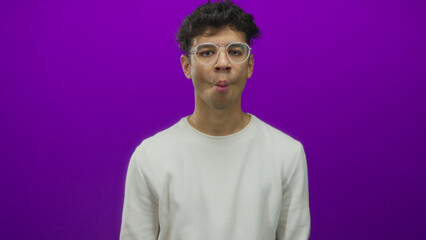 Hispanic man wearing round glasses and white shirt purses lips frontally in purple studio; contemplation.