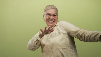 Woman smiling broadly with hands raised and playful gesture in studio against pale green backdrop; joy celebration energy.