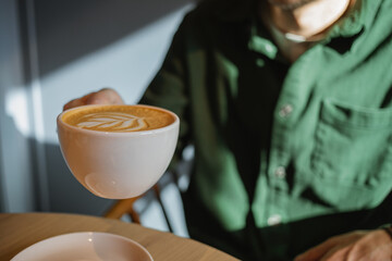 Close-up of a man drinking freshly brewed cappuccino in the morning sunshine at a cafe.