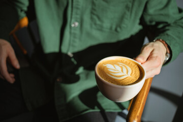 Close-up of a man enjoying a cup of freshly brewed cappuccino held in the warm morning sunshine at a cafe.