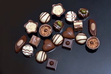 Close up of a gift selection of luxury chocolate, variety of shapes including a heart, florentines, and pistachios. White, milk and dark chocolate . They are against a grey black background.