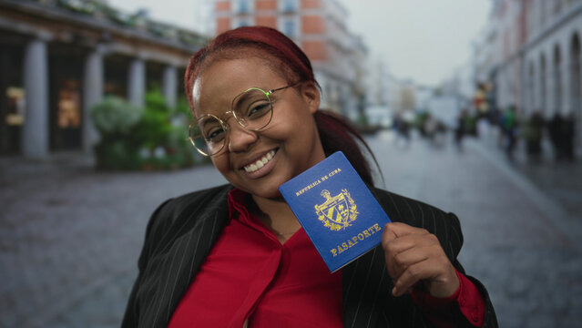 Woman wearing pinstripe jacket smiles while holding blue cuban passport on busy street; pride travel ambition.