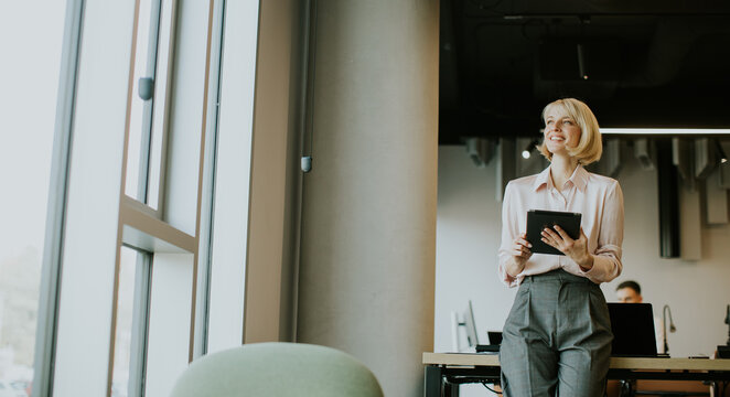 Businesswoman smiling while using tablet in modern office setting during daytime