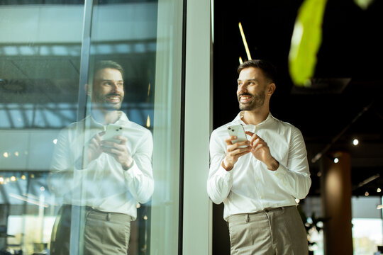 Man using smartphone while standing by a large window in a modern cafe setting