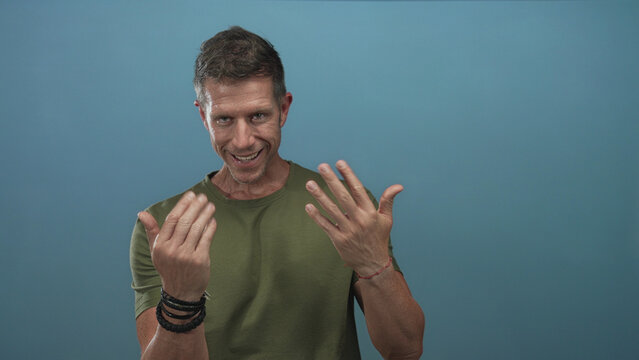 Man showing open palms and smiling in studio with blue backdrop and casual green shirt; friendly invitation.