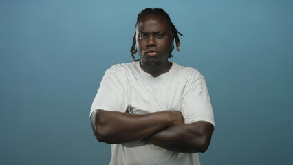 Man with crossed arms and visible forearms wearing a white tshirt in studio against a blue backdrop...