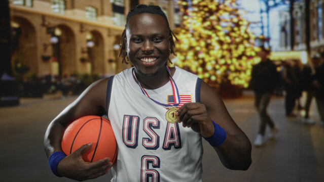 Man holds basketball and gold medal while smiling in a busy city street near a lit christmas tree wearing a usa basketball jersey; pride.