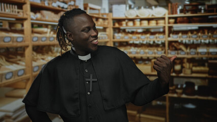 Fototapeta premium Man in clerical collar with cross necklace points thumb at shelves in building while smiling; welcoming joy.