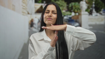 Hispanic woman gesturing timeout with hand wearing white shirt on city street displaying serious...