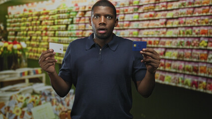Man holding two credit cards in raised hands while comparing white and blue cards in a supermarket...
