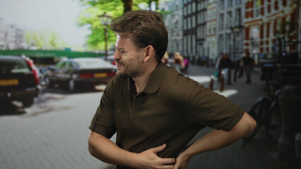 Fototapeta premium Man clutching right side and holding lower back on city street with backache near parked cars and bicycles; acute pain.