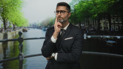 Man in suit with finger to cheek pensive pose on a street by an amsterdam canal; contemplation thought.
