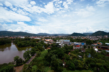Fototapeta premium Scenic Riverside Town with Hills and Vibrant Greenery Under a Bright Blue Sky