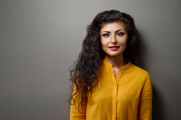A confident woman with long dark hair wears a vibrant yellow blouse against a neutral backdrop. This friendly, approachable portrait is ideal for lifestyle, fashion, or branding projects.