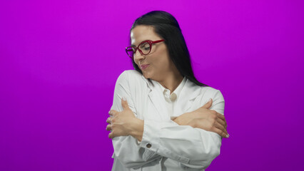 Hispanic woman in glasses and white shirt hugging herself against a vibrant pink wall, expressing joy and confidence in a colorful and uplifting setting.