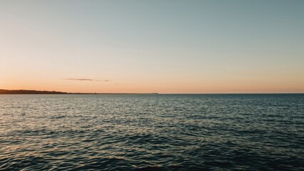 Naklejka premium A peaceful sea horizon at sunset or sunrise with calm waters and a distant shoreline.