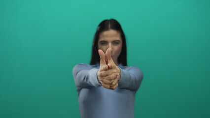 Woman playfully mimicking a gun gesture against a vibrant green background wearing a blue shirt...