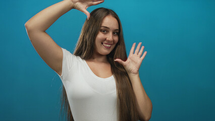 Woman in white t shirt framing face with both hands in blue studio; joy confidence self expression.