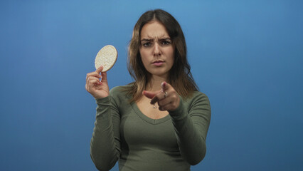 Woman holding a round rice cake with one hand and pointing finger at it with the other in blue...