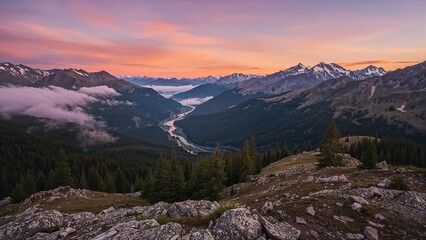 Vast mountain landscape at sunrise or sunset with snow-capped peaks, lush forests, and a river winding through the valley.
