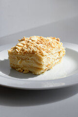 Plated slice of creamy, multi-layered pastry topped with a golden crumble. Dessert scene highlighting rich textures and light, indulgent sweetness perfect for bakery, cafe, or culinary features.