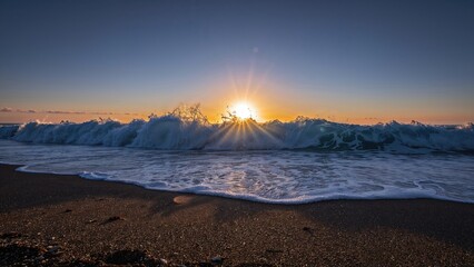 Fototapeta premium A sunset over the ocean with waves crashing onto the beach during sunset. The image captures the natural beauty and tranquility of a coastal scene.