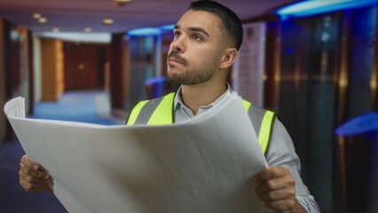 Man holds large blueprint with both hands and gazes upward in building hallway; concentration planning.