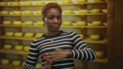 Woman makes time out gesture with hands inside cheese shop with rows of cheese wheels on wooden shelves; assertiveness.