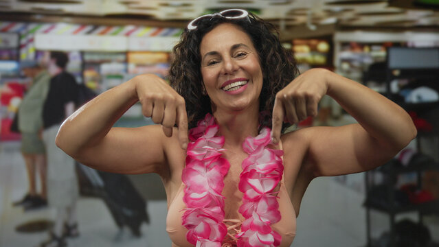 Hispanic woman with bare arms points index fingers downward in store; promotion discount invitation offer.