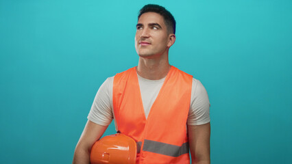 Man holding orange hard hat and wearing orange safety vest in studio against turquoise backdrop; safety professionalism optimism.