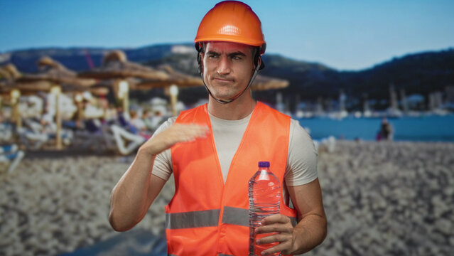 Man engineer in orange hardhat and high visibility vest holds plastic water bottle and wipes forehead in studio beach backdrop; thirst discomfort.