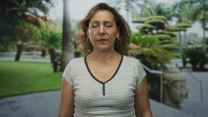 Woman closes eyes with calm posture on street flanked by lush palm trees and green lawn under soft...
