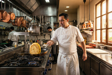 Cocinero profesional volteando tortilla de patatas en cocina industrial iluminada por luz natural