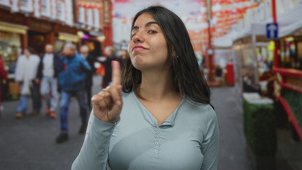 Hispanic woman wearing light blue top points finger to chest on bustling street with determined stare; refusal.