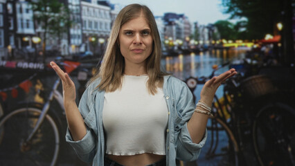 Blonde woman stands with arms at back and closes eyes by canal on street in amsterdam at dusk; serenity.