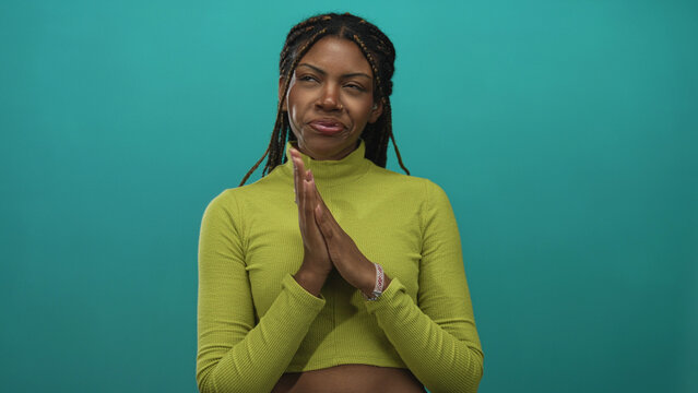 Woman steepling hands in lime turtleneck against teal studio wall with braids and visible rings, smirking expression; mischief intent. - Powered by Adobe