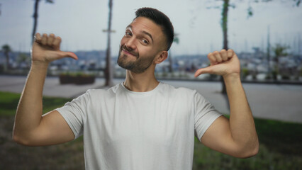 Young man outdoors pointing to himself with thumbs in an urban city street setting, capturing a...