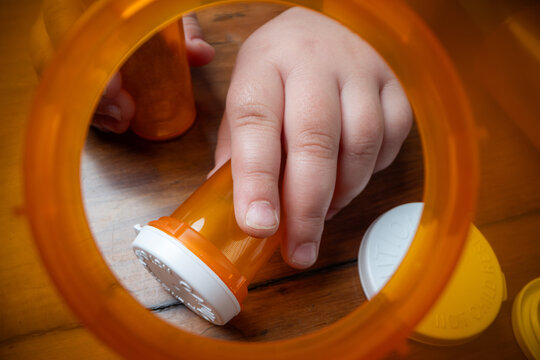 A powerful conceptual photograph showing a child's hand reaching for colorful, unattended prescription pills or medication.