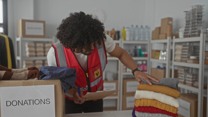 Man sorting donated clothing into a labeled donations box in a charity building while writing on a clipboard; community service compassion.