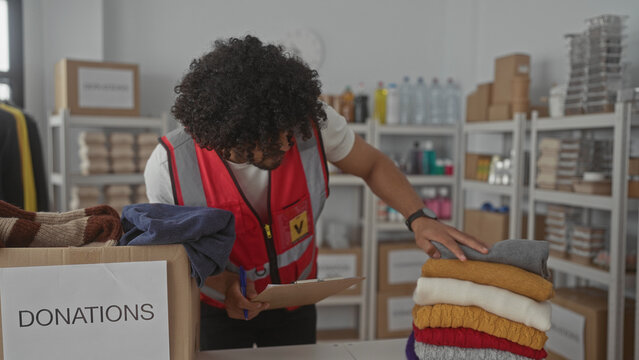 Man sorting donated clothing into a labeled donations box in a charity building while writing on a clipboard; community service compassion.