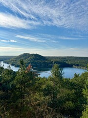 Obraz premium Scenic view over the hills, lake, and forest at Connecterra Maasmechelen on a clear day. Lush nature, blue sky, and panoramic landscape.