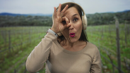 Naklejka premium Woman wearing headphones gestures playfully in a green park setting, showcasing positive expressions in an outdoor atmosphere.