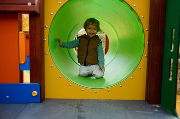 Happy Child Plays In Colorful Playground Tunnel On Autumn Day, Smiling And Exploring