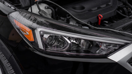 Foggy inside wet headlight of a modern black car. Open hood. Headlight repair. Headlight depressurization. Broken headlight