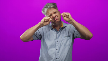 Man rubbing eyes with fists, forearms visible wearing a short sleeve button shirt in studio; sadness fatigue.