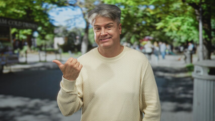 Naklejka premium Man points thumb over shoulder on street, wearing beige sweater with a resigned, slight grimace; resignation.