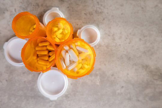 An overhead flat lay shot showing a mass or collection of pills and various open prescription bottles scattered on a surface.