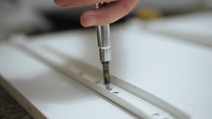 Tightening screw on drawer slide during dresser assembly. Fastening hardware on drawer rail while building furniture. Securing metal guide on cabinet panel during woodworking project